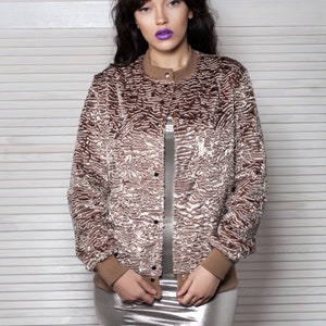 Puede incluir: Chaqueta bomber de piel sint&eacute;tica marr&oacute;n y crema con cuello redondo y cierre de botones. La chaqueta tiene pu&ntilde;os acanalados marrones y un cuello a juego. La modelo lleva un vestido plateado metalizado.