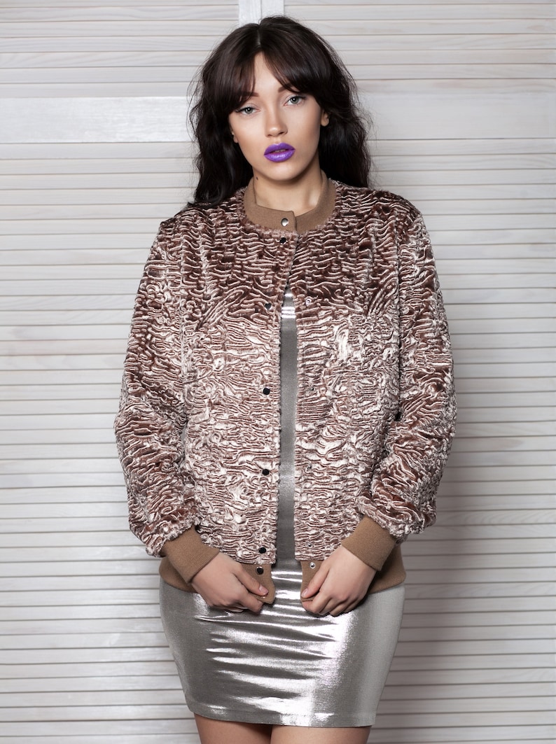Puede incluir: Chaqueta bomber de piel sint&eacute;tica marr&oacute;n y crema con cuello redondo y cierre de botones. La chaqueta tiene pu&ntilde;os acanalados marrones y un cuello a juego. La modelo lleva un vestido plateado metalizado.