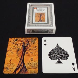 May include: A deck of playing cards with a tree design on the back of the cards. One card shows the Ace of Spades. The deck is in a white box with a clear window, displaying a card with a tree image.