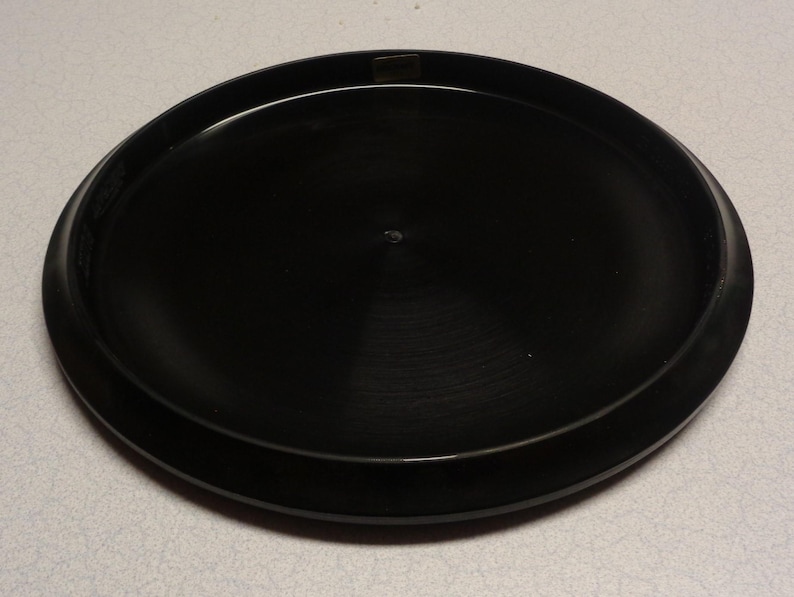 May include: A black disc golf disc with a smooth, circular design. The disc has a slightly raised rim and a flat center. The disc is made of a durable plastic material and is designed for outdoor use. The disc is approximately 8.5 inches in diameter.