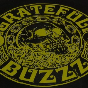 May include: Black graphic with the words "Grateful Buzz" in a yellow, circular design. The design includes a skull, roses, and chain links. The text "MICHAEL BARNARD" is also visible.