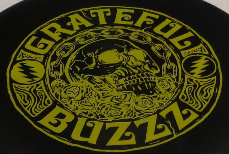 May include: Black graphic with the words "Grateful Buzz" in a yellow, circular design. The design includes a skull, roses, and chain links. The text "MICHAEL BARNARD" is also visible.