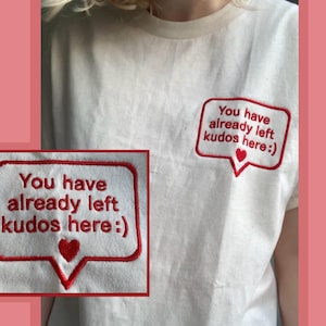 May include: Off-white t-shirt featuring a red embroidered speech bubble. The bubble design includes the text "You have already left kudos here:)" and a small red heart. The design is repeated on the shirt.