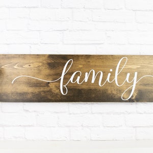 May include: A wooden sign with the word "family" written in white cursive script. The sign is dark brown and has a rustic look.