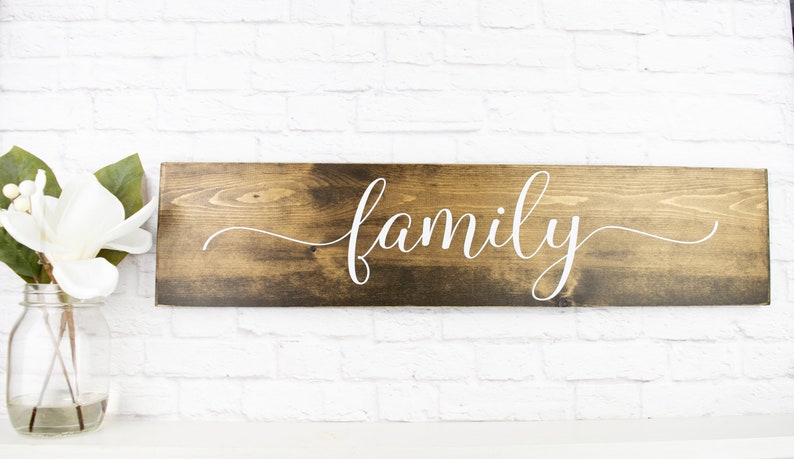 May include: A wooden sign with the word "family" written in white cursive script. The sign is dark brown and has a rustic look.