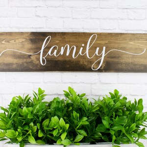 May include: A wooden sign with the word "family" written in white cursive script on a dark brown background.