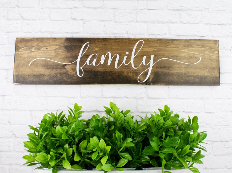 May include: A wooden sign with the word "family" written in white cursive script on a dark brown background.
