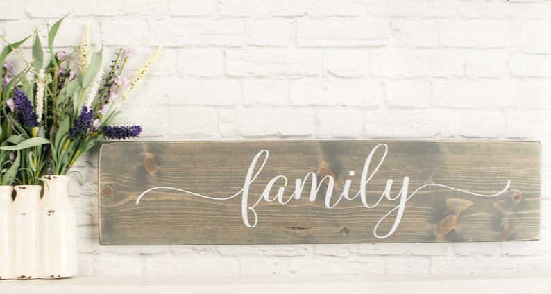 May include: A gray wooden sign with the word "family" written in white cursive script.