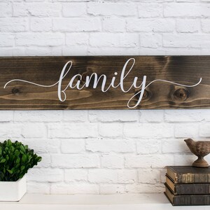 May include: A wooden sign with the word "family" written in white cursive script on a dark brown background.