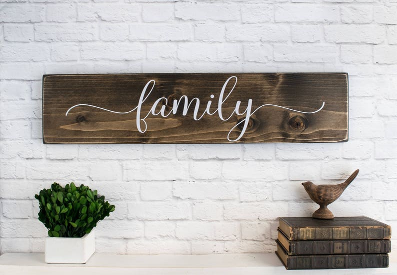 May include: A wooden sign with the word "family" written in white cursive script on a dark brown background.