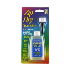 May include: A clear plastic bottle of Zip Dry Paper Glue with a black applicator tip. The bottle is labeled with the product name, "Zip Dry Paper Glue", and lists features such as "Fast Drying Glue for Paper Arts", "Acid and Lignin Free", "Wrinkle Free", and "Dries Clear". The bottle is 2 fl oz (59.15 ml).