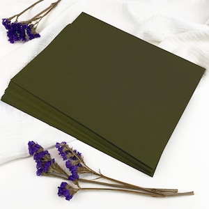 May include: A stack of dark green cardstock paper on a white surface with purple flowers.