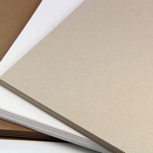 May include: Three sheets of paper, one brown, one white and one beige, stacked on top of each other.