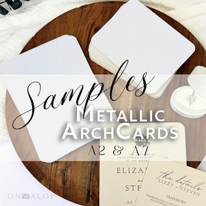 May include: A collection of white metallic arch cards in A2 and A7 sizes, featuring a smooth finish. The cards are displayed alongside a small white ring box containing a ring. Text on the image reads Samples METALLIC ARCHCARDS A2 & A7.