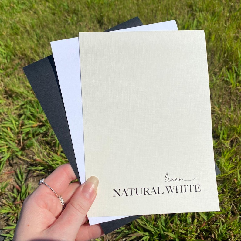 May include: Three sheets of paper, one black, one white, and one off-white with a linen texture. The off-white sheet has the text "linen NATURAL WHITE" printed on it.