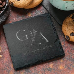 May include: Black slate coaster with a white engraved design of the letters G and A with a floral motif. The text "Giselle & Andrew | May 25, 2026" is also engraved on the coaster.
