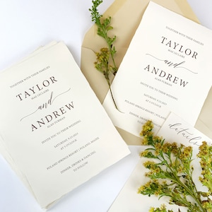 May include: Ivory wedding invitations with the names "Taylor and Andrew" in elegant script. The invitations include details about the wedding date, time, and location. Greenery and a cream-colored envelope are also visible.