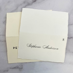 May include: A white place card with the name "Stephanie Anderson" written in black cursive script. The number "8" is printed in black in the top right corner.