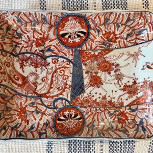 May include: Rectangular ceramic serving dish with a detailed floral and bird design. The dish features a white base with intricate patterns in red, orange, and blue. The design includes flowers, birds, and stylized foliage, creating a decorative and artistic piece.