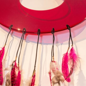 May include: A red glass dreamcatcher with pink and white feathers hanging from it.