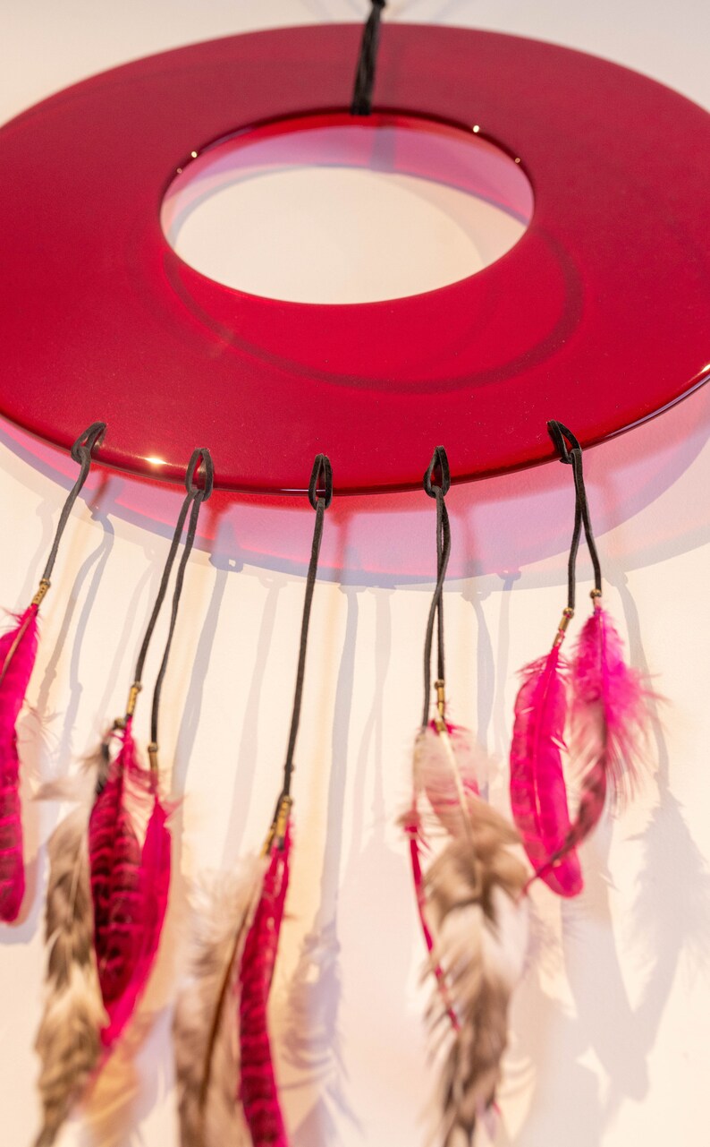 May include: A red glass dreamcatcher with pink and white feathers hanging from it.