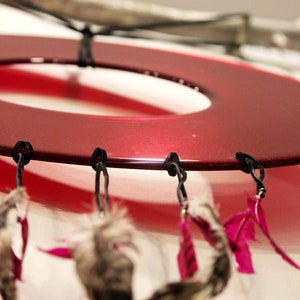 May include: A red circular dreamcatcher with black strings and pink feathers hanging from it.