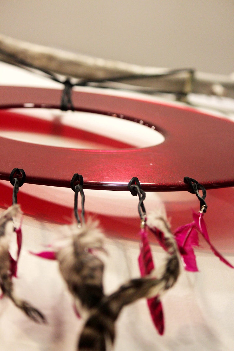 May include: A red circular dreamcatcher with black strings and pink feathers hanging from it.