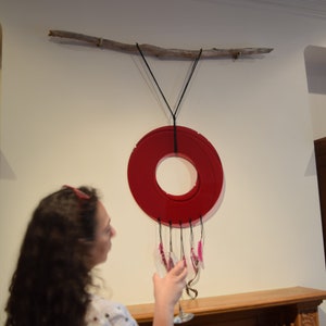May include: A red circular glass mobile hangs from a branch attached to the wall. The mobile has a ring of pink glass pieces hanging from it.