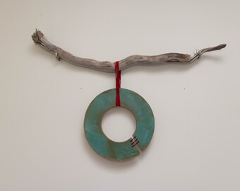 May include: A teal ceramic ring with red stitching hangs from a driftwood branch with red string.