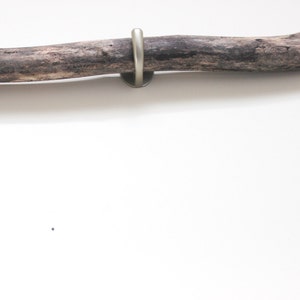 May include: A rustic wooden branch with a metal hook attached to the end. The branch is a natural brown color and has a rough texture.
