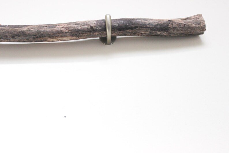 May include: A rustic wooden branch with a metal hook attached to the end. The branch is a natural brown color and has a rough texture.