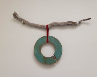 May include: A teal ceramic ring with red stitching hangs from a driftwood branch with red string.