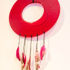 May include: A red circular dreamcatcher with pink and brown feathers hanging from it.