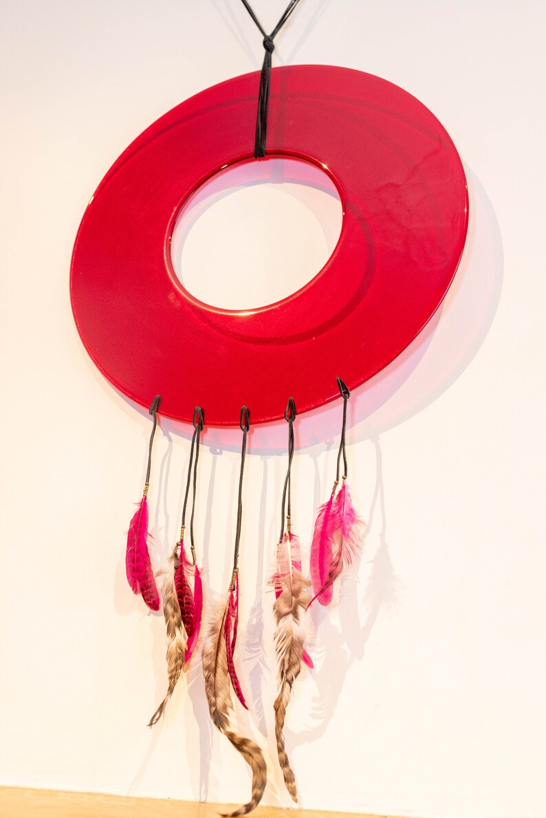 May include: A red circular dreamcatcher with pink and brown feathers hanging from it.