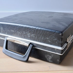 May include: A black vinyl record carrying case with a silver trim and a black handle. The case has a worn, vintage look.