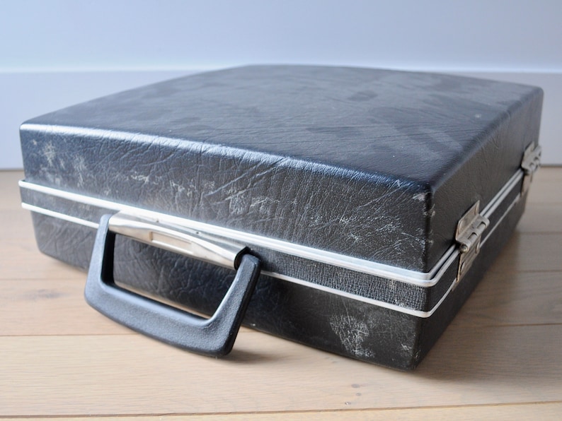 May include: A black vinyl record carrying case with a silver trim and a black handle. The case has a worn, vintage look.