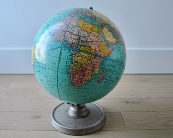 May include: A vintage blue globe with a metal stand. The globe features a map of the world with continents in different colors. The globe is on a wooden surface.