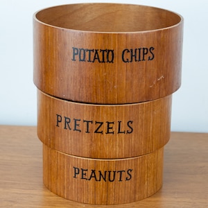 Peut inclure: Trois bols en bois empilés les uns sur les autres. Le bol du haut indique "Potato Chips", le bol du milieu indique "Pretzels" et le bol du bas indique "Peanuts".