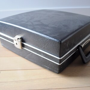 May include: A black vinyl record carrying case with a silver latch and a black handle.