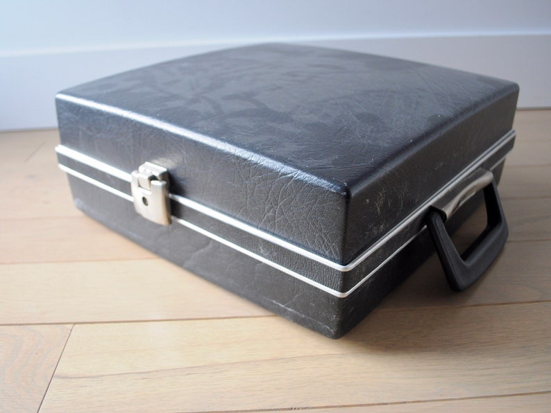 May include: A black vinyl record carrying case with a silver latch and a black handle.