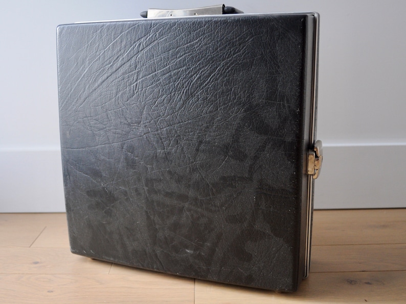 May include: A black leather briefcase with a silver metal frame and a silver metal latch. The briefcase has a textured surface.