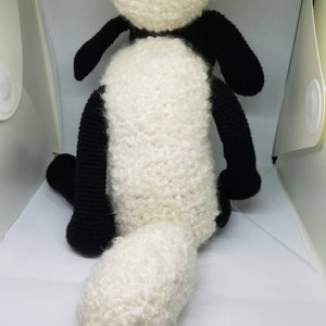 Puede incluir: Un juguete de peluche de oveja de crochet negro y blanco con una cola blanca esponjosa.