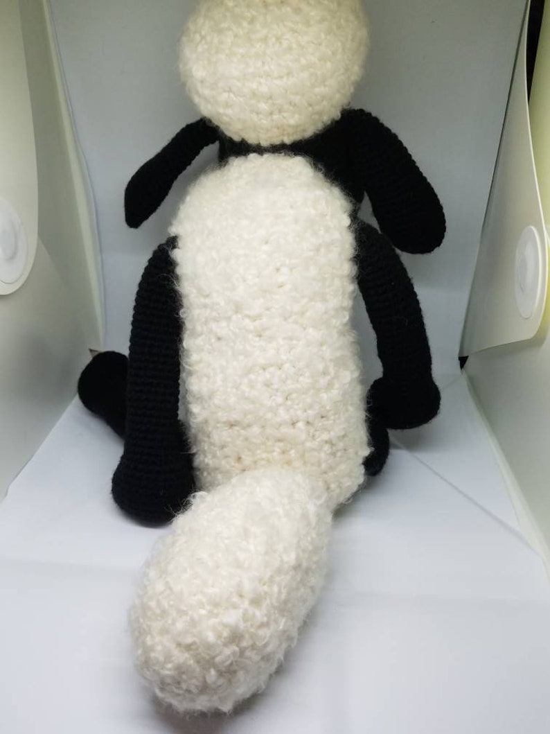 Puede incluir: Un juguete de peluche de oveja de crochet negro y blanco con una cola blanca esponjosa.