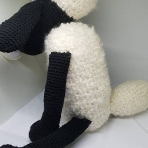 Puede incluir: Un juguete de peluche de oveja de crochet blanco y negro. La oveja tiene la cara, las patas y la cola negras. El cuerpo es blanco y esponjoso.