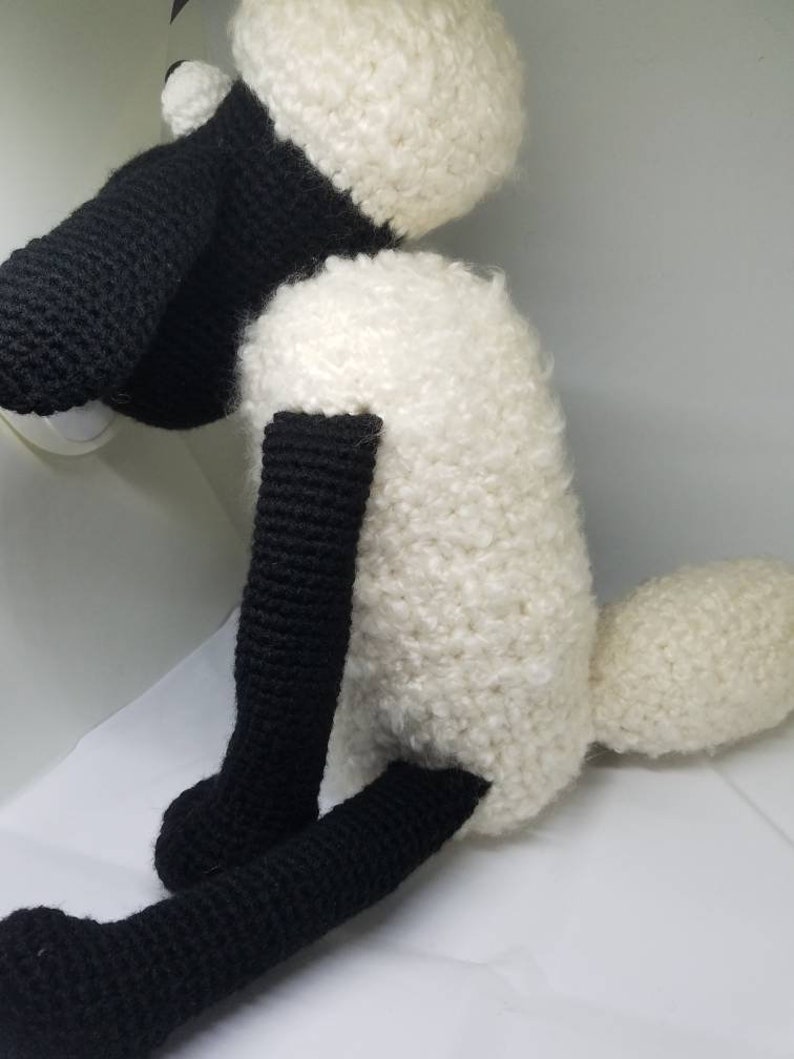 Puede incluir: Un juguete de peluche de oveja de crochet blanco y negro. La oveja tiene la cara, las patas y la cola negras. El cuerpo es blanco y esponjoso.