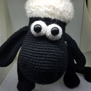 Puede incluir: Un juguete de peluche de oveja de crochet negro y blanco con grandes ojos negros. La oveja tiene una cabeza blanca y esponjosa y un cuerpo negro.