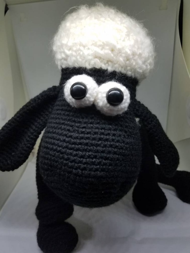 Puede incluir: Un juguete de peluche de oveja de crochet negro y blanco con grandes ojos negros. La oveja tiene una cabeza blanca y esponjosa y un cuerpo negro.