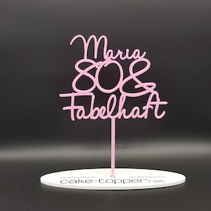 Könnte beinhalten: Rosa Acryl-Kuchentopper mit dem Text "Maria 80 & Fabelhaft" und einem weißen Sockel mit dem Text "cake-topper.net".