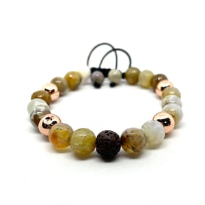 May include: A bracelet with a mix of agate beads in earthy tones, rose gold-coloured metal beads, and a dark brown lava bead. The bracelet is adjustable with a black cord. The beads are approximately 1 cm in diameter.
