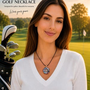 May include: A woman wearing a glitter golf necklace with a circular pendant. The pendant has a central white stone surrounded by colorful gems. The necklace is on a black cord. The text "GLITTER GOLF NECKLACE" is at the top of the image.